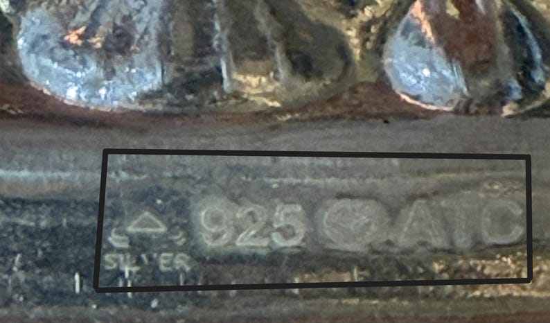 Puede incluir: Primer plano de un objeto de metal plateado con la inscripci&oacute;n "STER 925 CATO" en la parte inferior.