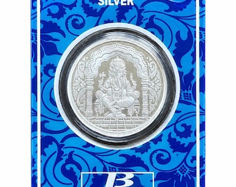 Könnte beinhalten: Eine runde Silbermünze mit einem geprägten Bild von Ganesha, der unter einem Bogen sitzt, eingeschlossen in einer klaren Schutzkapsel. Die Münze ist auf einer leuchtend blauen rechteckigen Karte mit Blumenmustern, dem Text SILVER und dem Logo BANGALORE REFINERY www.brpl.asia montiert.