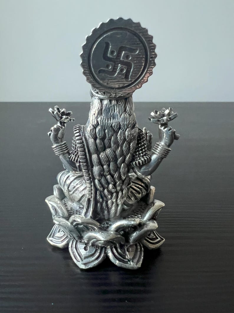 Op de afbeelding: Zilveren beeld van een hindoe&iuml;stische godin die op een lotusbloem zit. De godin draagt een traditionele sari en heeft een halo met een swastika-symbool boven haar hoofd.