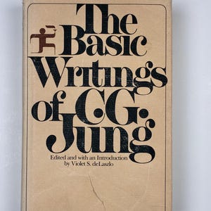 May include: A vintage book titled "The Basic Writings of C.G. Jung" with a tan cover and black lettering. The book is edited by Violet S. deLaszlo and published by Modern Library. The cover features a stylized graphic above the title.