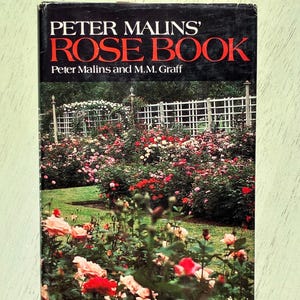 May include: A hardcover book titled Peter Malins' Rose Book by Peter Malins and M.M. Graff. The black dust jacket features white and red text at the top and a full-color photograph of a lush rose garden with a white trellis in the background.