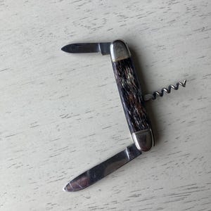 May include: A brown and black handled pocket knife with a corkscrew, a small blade, and a larger blade.