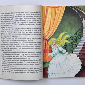 Może przedstawiać: Otwarta książka dla dzieci z ilustracją Kopciuszka w białej sukni z niebieskim stanikiem i długimi blond włosami. W tle schody i zasłony.