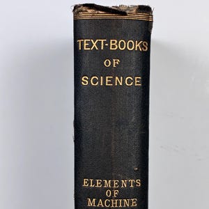 May include: A close-up of a vintage black book spine with gold lettering. The text reads "TEXT-BOOKS OF SCIENCE" and "ELEMENTS OF MACHINE DESIGN" with the author's name, UNWIN, at the bottom. The book's edges show signs of wear.