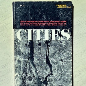 May include: A paperback book titled CITIES, a Scientific American book. The cover features a black and white aerial photograph of a city grid and waterways. Text reads: Why urbanization of the world population raises the most serious domestic questions.