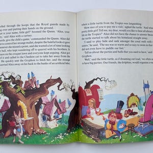 Może przedstawiać: Otwarta książka z kolorowymi ilustracjami z bajki dla dzieci. Jedna strona przedstawia kr&oacute;lika serwującego herbatę, druga przyjęcie herbaciane z Alicją. Widoczny jest tekst.