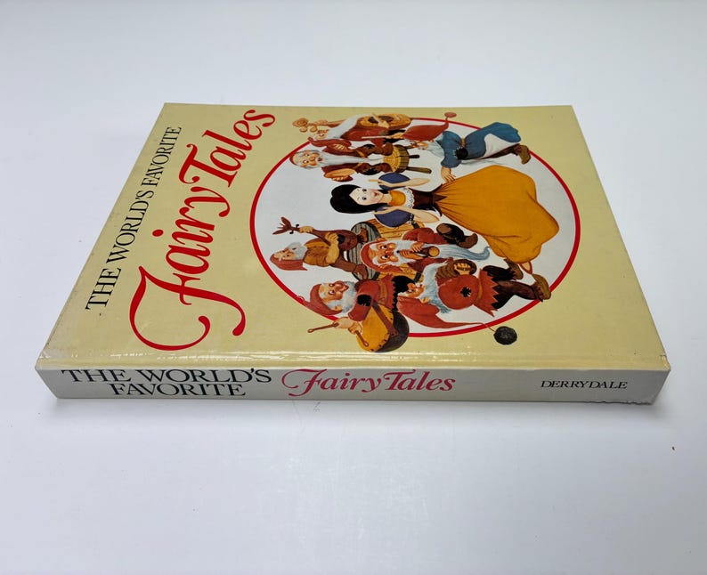 Może przedstawiać: Twarda oprawa książki zatytułowana "The World's Favorite Fairy Tales". Okładka przedstawia ilustrację Kr&oacute;lewny Śnieżki i Siedmiu Krasnoludk&oacute;w w czerwonym okręgu. Książka ma kremowe tło, a tytuł jest w ozdobnej czcionce.