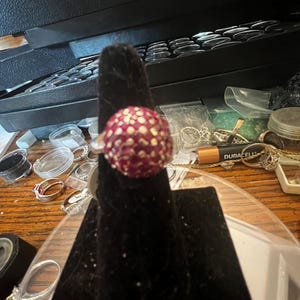 Może przedstawiać: Srebrny pierścionek z dużym, okrągłym, różowym kamieniem szlachetnym osadzonym w teksturowanej oprawie. Kamień szlachetny jest pokryty małymi, białymi kamieniami.