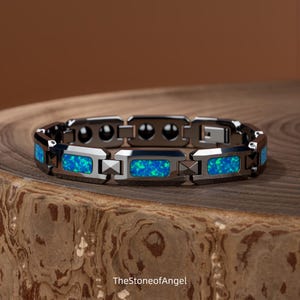 May include: A dark metallic link bracelet featuring rectangular inlays of vibrant blue and green iridescent stone. The bracelet has a polished finish with alternating dark metal segments and includes the text TheStoneofAngel at the bottom.
