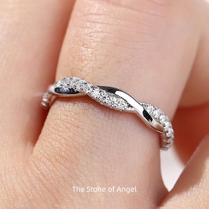 May include: A silver ring with a twisted design, set with small, sparkling gemstones. The ring is on a finger, highlighting its intricate details. The text "The Stone of Angel" is visible at the bottom of the image.