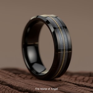 May include: A black ring with a glossy finish. The ring features a central band with a gold-colored, string-like design encased in a clear material. The ring is set against a wooden surface. The text "The Stone of Angel" is at the bottom.