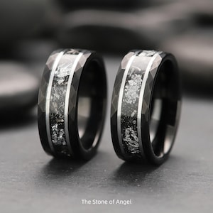 Può includere: Due anelli neri con intarsio argentato e design sfaccettato. Gli anelli hanno una fascia argentata al centro con un intarsio scuro strutturato. Gli anelli sono su uno sfondo scuro. Il testo in basso recita "The Stone of Angel".