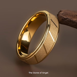 Könnte beinhalten: Ein goldfarbener Ring mit strukturiertem Band und geometrischem Design. Der Ring hat eine glatte, polierte Innenseite und eine matte Oberfläche auf dem äußeren Band. Der Text "The Stone of Angel" befindet sich unten im Bild.