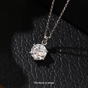 May include: A silver necklace with a large, round, clear gemstone pendant. The pendant is set in a six-prong setting and sparkles brightly. The chain is delicate and hangs from the pendant. The text "The Stone of Angel" is at the bottom.