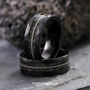 May include: Two black rings with a hammered finish and a silver string inlay. The rings are stacked on top of each other, with the text "TheStoneofAngel" visible at the bottom.