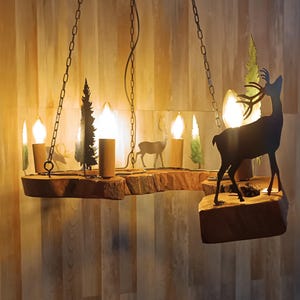 Può includere: Un lampadario rustico con una base in legno con silhouette decorative di cervi e alberi in metallo. L'apparecchio include diverse lampadine in stile Edison ed è sospeso da catene. Il design generale evoca un tema boschivo.