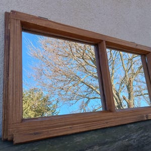 Könnte beinhalten: Ein Spiegel mit Holzrahmen und zwei Glasscheiben. Der Spiegel spiegelt einen blauen Himmel und Bäume wider.