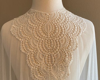 May include: A white crochet lace collar with a scalloped edge, attached to a sheer white tulle fabric.