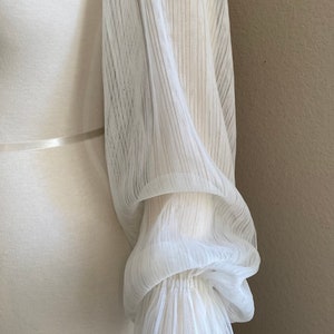 Puede incluir: Una manga blanca y transparente con pu&ntilde;o plisado. La manga est&aacute; hecha de una tela ligera y texturizada con l&iacute;neas verticales. El pu&ntilde;o est&aacute; recogido y tiene un borde con volantes. La manga est&aacute; unida a una prenda blanca.