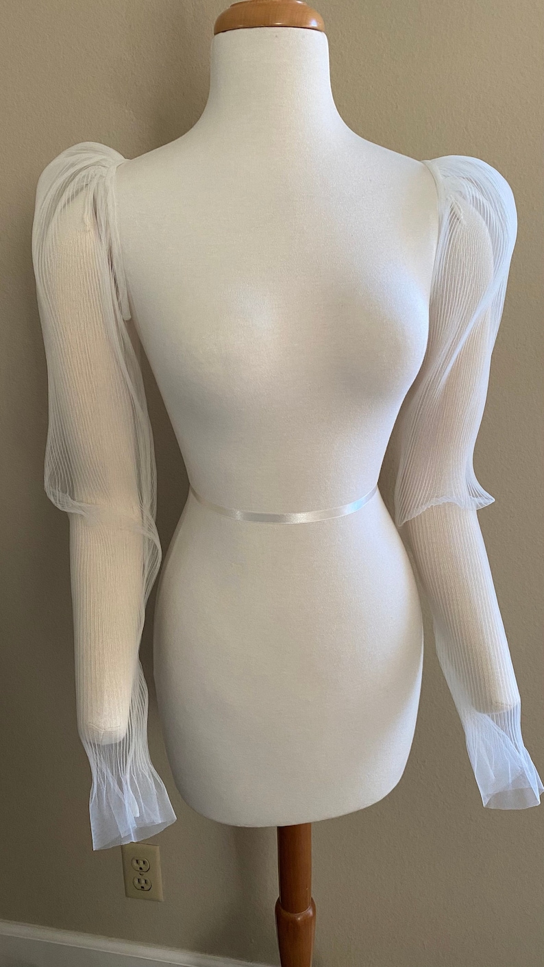 May include: White sheer fabric sleeves with a gathered puff at the shoulder. The sleeves are on a white dress form.