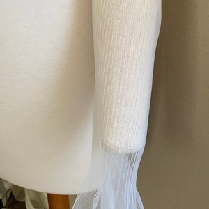 May include: White sheer fabric with a ruffled edge. The fabric is delicate and has a fine mesh texture.