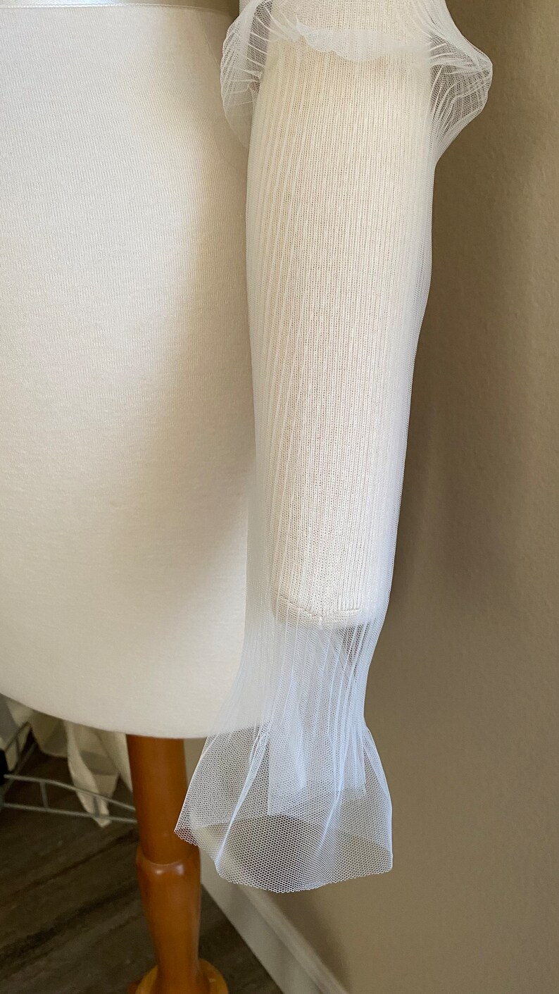 May include: White sheer fabric with a ruffled edge. The fabric is delicate and has a fine mesh texture.