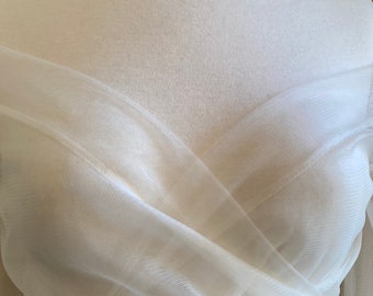 May include: White off-the-shoulder tulle top with a criss-cross design in the front. The top is made of a sheer fabric and has a relaxed fit.