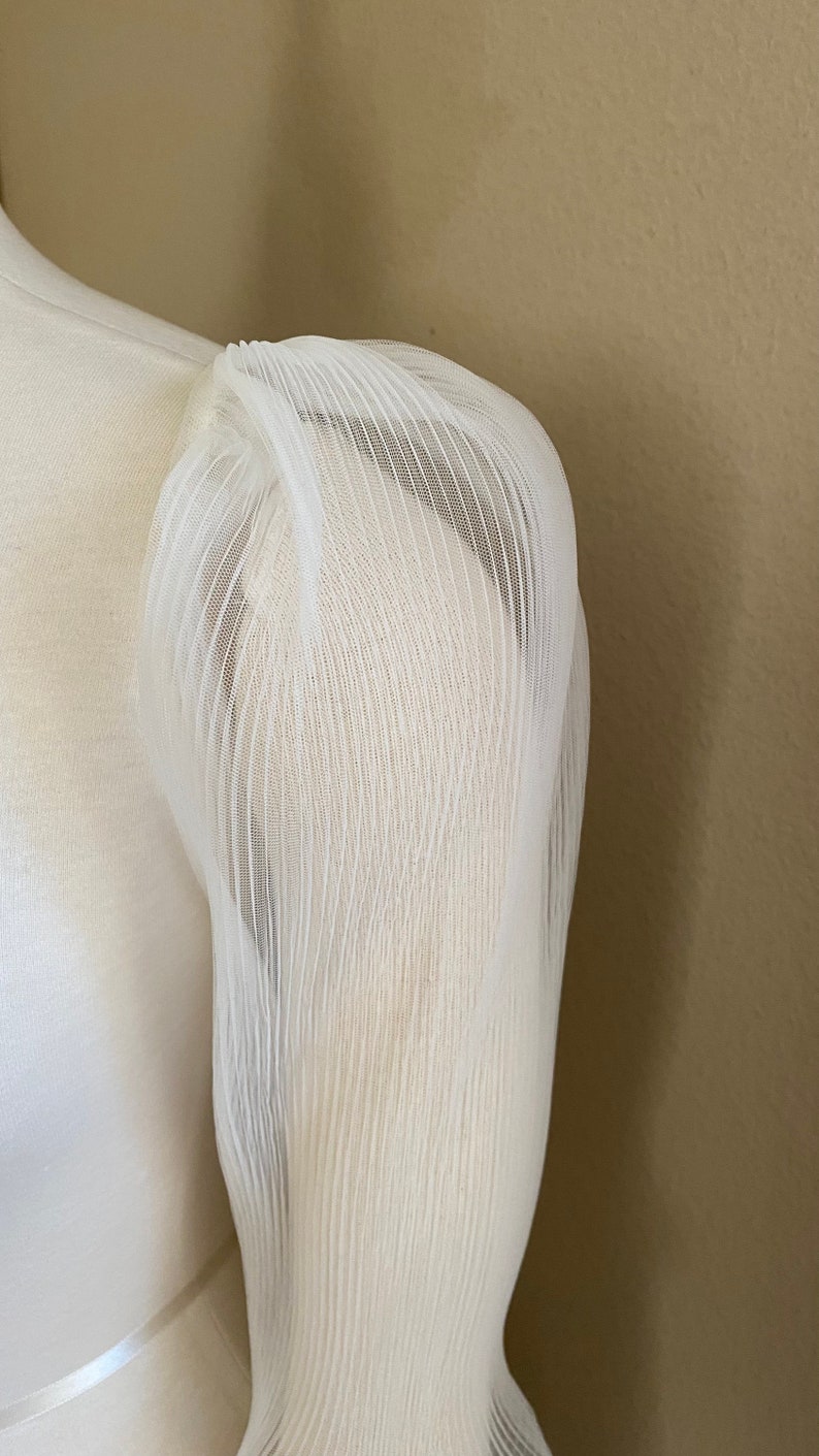 May include: White sheer fabric with a pleated texture. The fabric is gathered at the top and has a loose, flowing shape.
