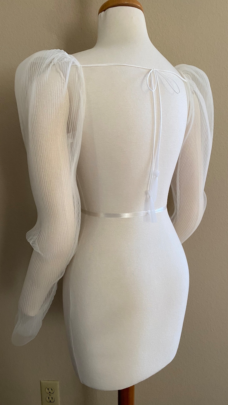 May include: White sheer top with puffed sleeves and a tie at the back.