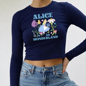 A woman wearing a navy blue crop top with a graphic design featuring a character from the "Alice in Wonderland" series.