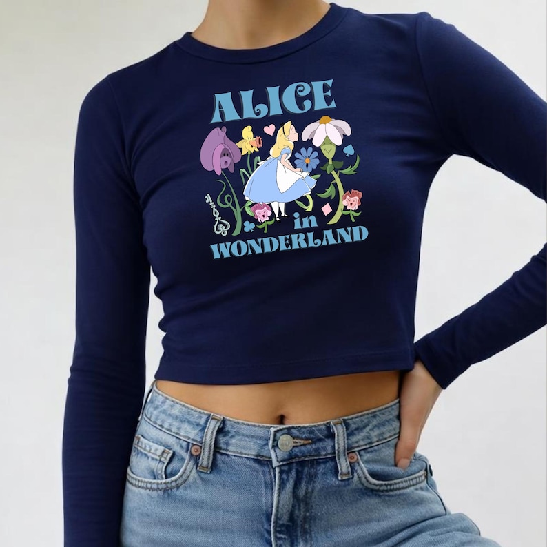 A woman wearing a navy blue crop top with a graphic design featuring a character from the "Alice in Wonderland" series.