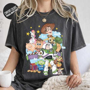 A person wearing a gray t-shirt with a colorful graphic of characters from the Toy Story movie, including Woody, Buzz Lightyear, and other beloved characters.