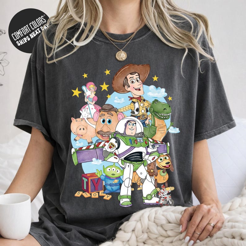 A person wearing a gray t-shirt with a colorful graphic of characters from the Toy Story movie, including Woody, Buzz Lightyear, and other beloved characters.