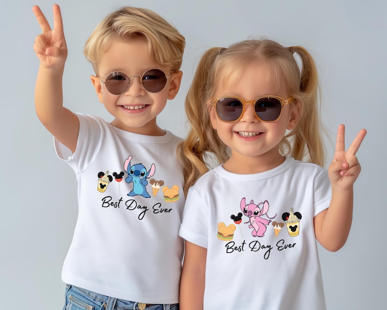 Two young children wearing white t-shirts with the text "Best Day Ever" and cartoon characters, smiling and making a peace sign gesture.