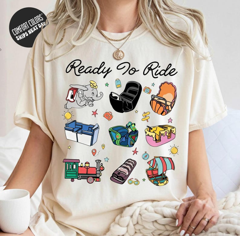 A woman wearing a white t-shirt with a graphic design featuring various cartoon-style illustrations of different objects and activities, along with the text "Ready to Ride".