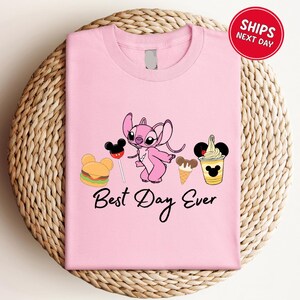 A pink t-shirt with a cartoon character and various Disney-themed items, such as a Mickey Mouse, a hamburger, and a milkshake, along with the text "Best Day Ever".