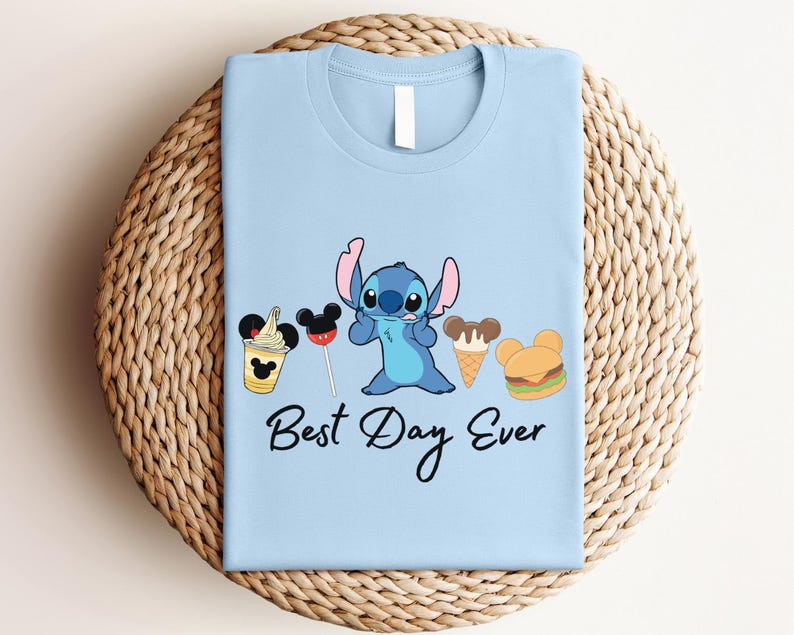 A light blue t-shirt with a cartoon character and various Disney-themed items, such as Mickey Mouse and a hamburger, along with the text "Best Day Ever".