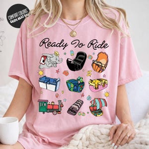 A woman wearing a pink t-shirt with various cartoon-style illustrations of objects and characters, including a train, a boat, and a person.
