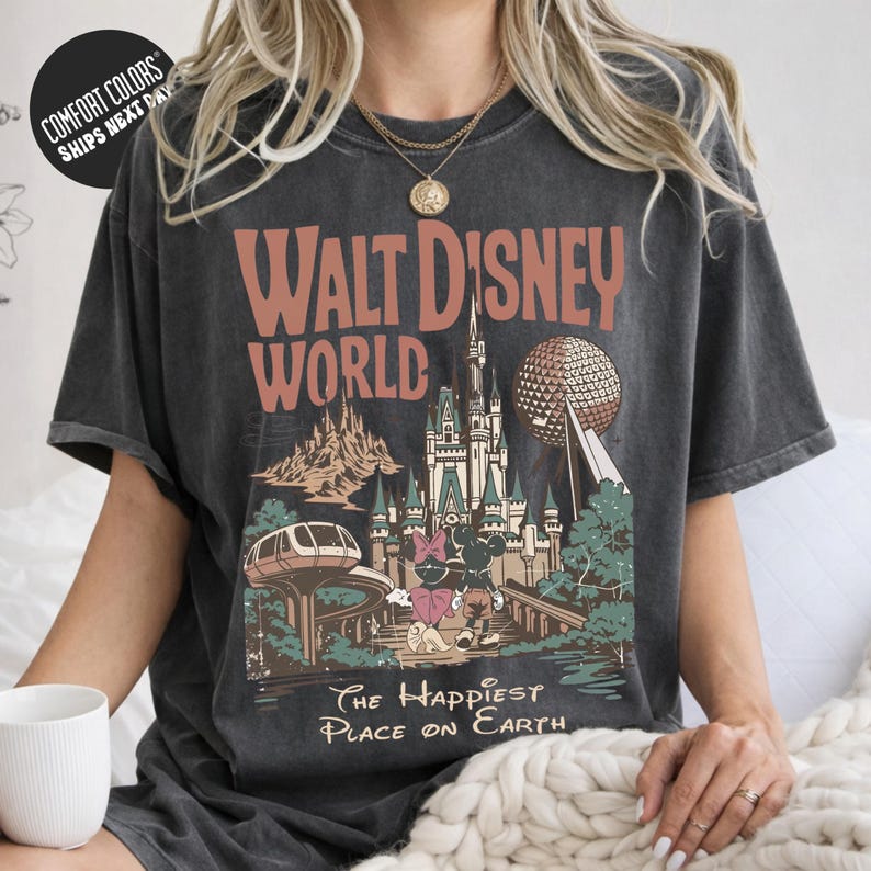 A person wearing a gray t-shirt with a graphic design of Disney World, including a castle, roller coaster, and other iconic landmarks.
