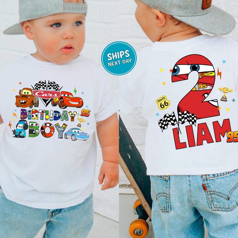 A young child wearing a white t-shirt with a Cars-themed birthday design, including the character "Liam" and the number "2". The child is also wearing a gray baseball cap and blue jeans.
