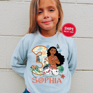 A young girl wearing a light blue sweater with a graphic of a character from the movie "Moana" and the text "Sophia" printed on it.