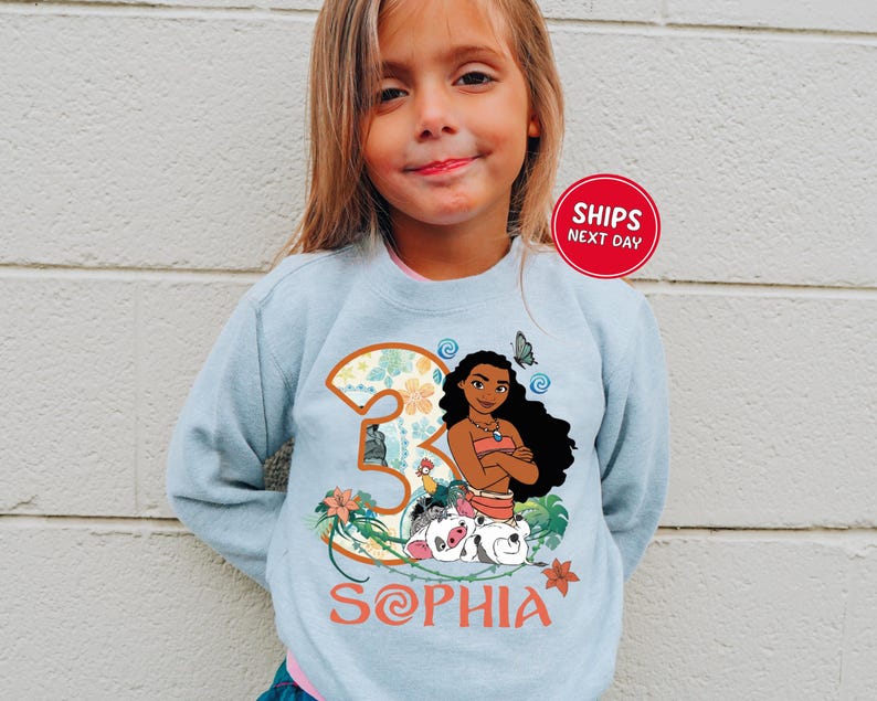 A young girl wearing a light blue sweater with a graphic of a character from the movie "Moana" and the text "Sophia" printed on it.