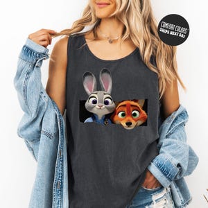 A woman wearing a gray tank top with a graphic of two cartoon animal characters, a rabbit and a fox, peeking out from a hole.