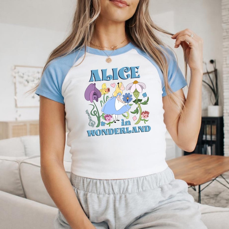 A woman wearing a white and blue t-shirt with a graphic design of Alice in Wonderland.