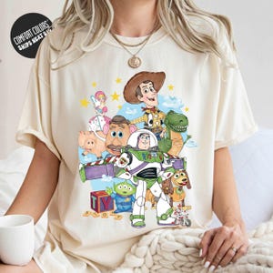 A person wearing a white t-shirt with a colorful graphic of characters from the Toy Story movie, including Woody, Buzz Lightyear, and other beloved characters.