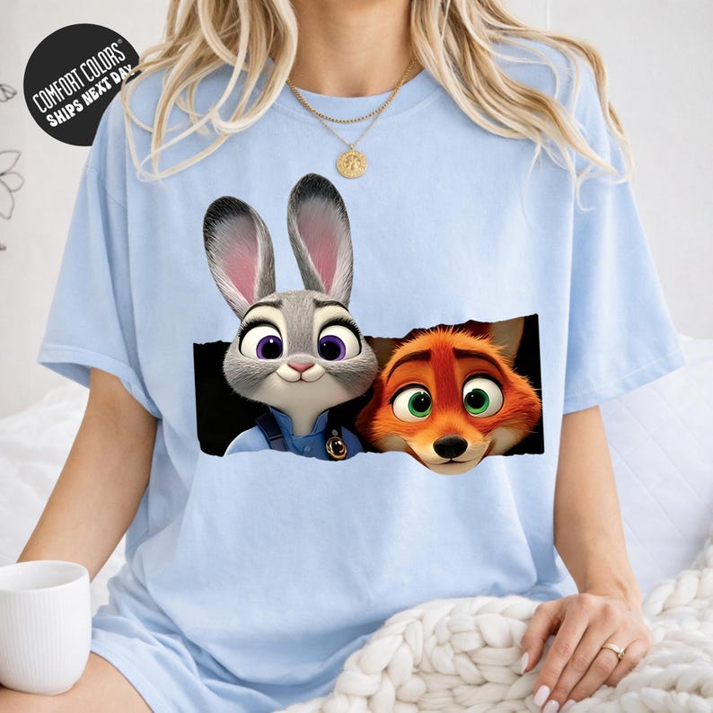 A woman wearing a light blue t-shirt with a graphic of a rabbit and a fox peeking out from behind a black hole.