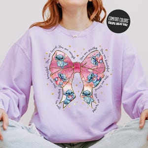 A person wearing a purple sweater with a large bow and various cartoon characters printed on it.
