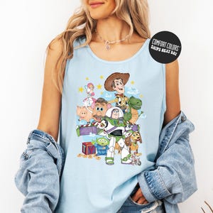A woman wearing a light blue tank top with a graphic of characters from the Toy Story franchise, including Woody, Buzz Lightyear, and other beloved characters.