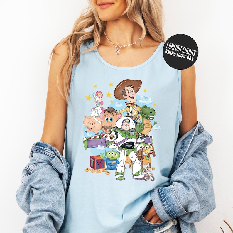 A woman wearing a light blue tank top with a graphic of characters from the Toy Story franchise, including Woody, Buzz Lightyear, and other beloved characters.