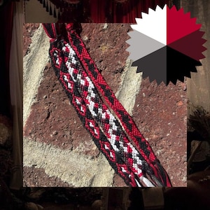 May include: A woven friendship bracelet featuring a geometric pattern in black, white, and red thread. The design consists of repeating diamond and zigzag shapes created with intricate knotting techniques, ending in loose braided ties at both ends.